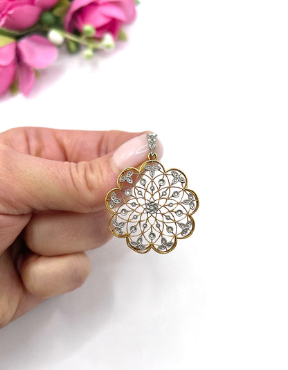 A floral openwork diamond pendant in gold and platinum, held in a hand