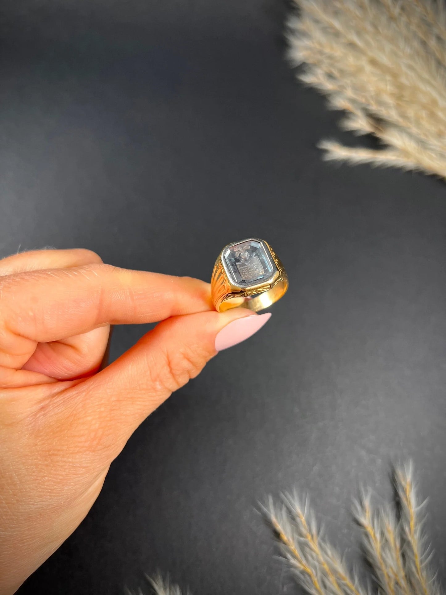 A yellow gold blue glass intaglio signet ring, held in a hand