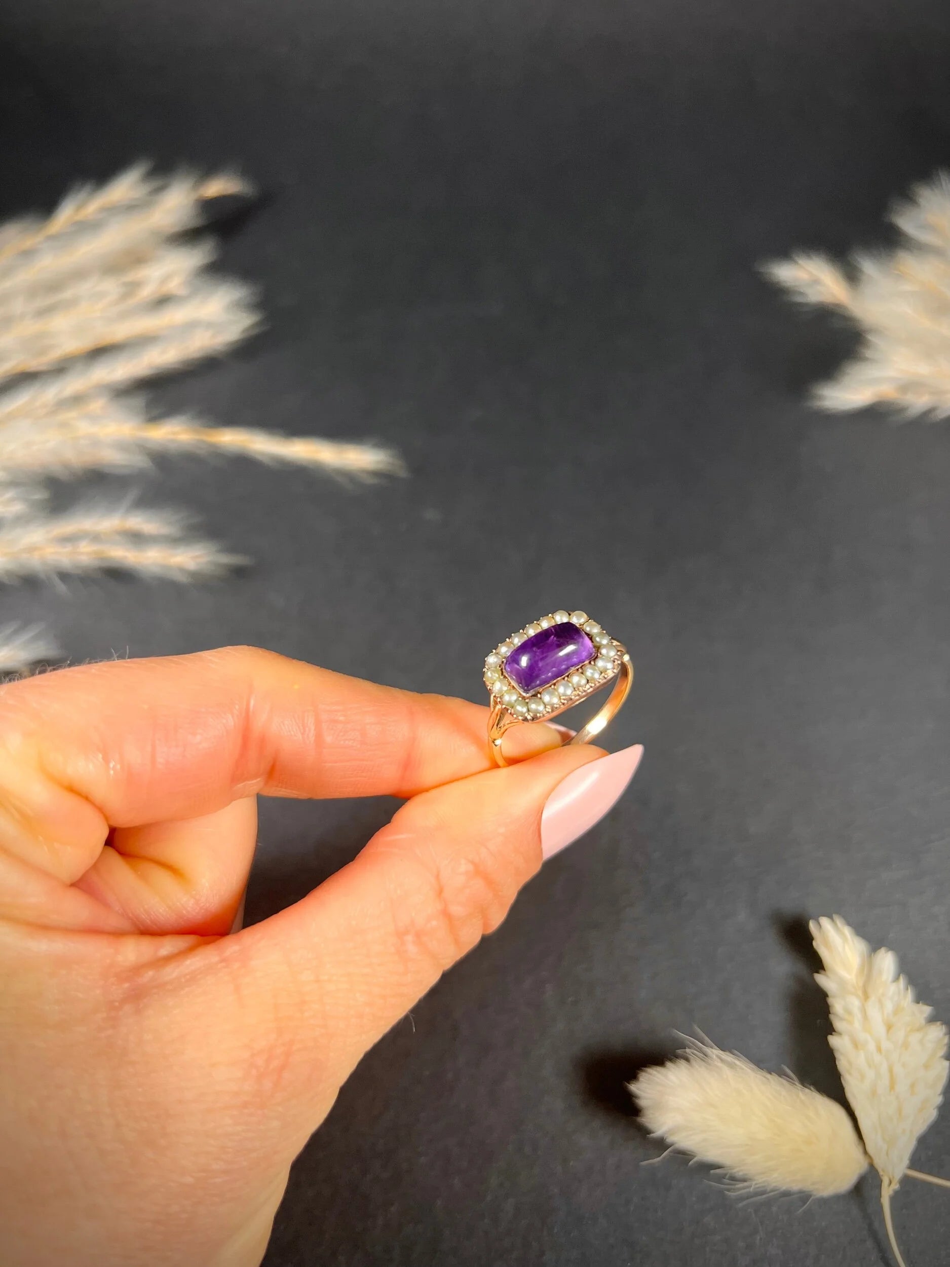 A cabochon amethyst and pearl halo cluster ring in gold, held in a hand
