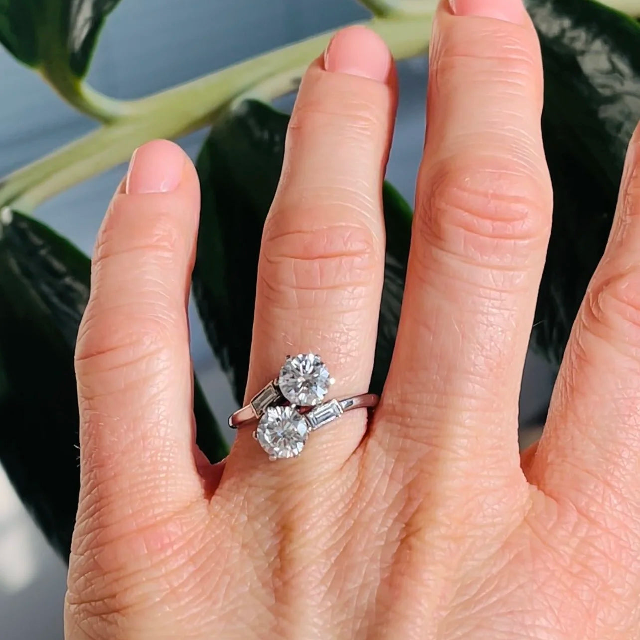 A two stone diamond crossover ring in white gold with diamond shoulders, modelled on the ring finger of a hand