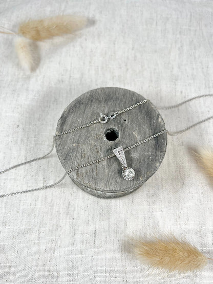 An old cut diamond pendant in white metal with a matching chain, on a circular wooden object