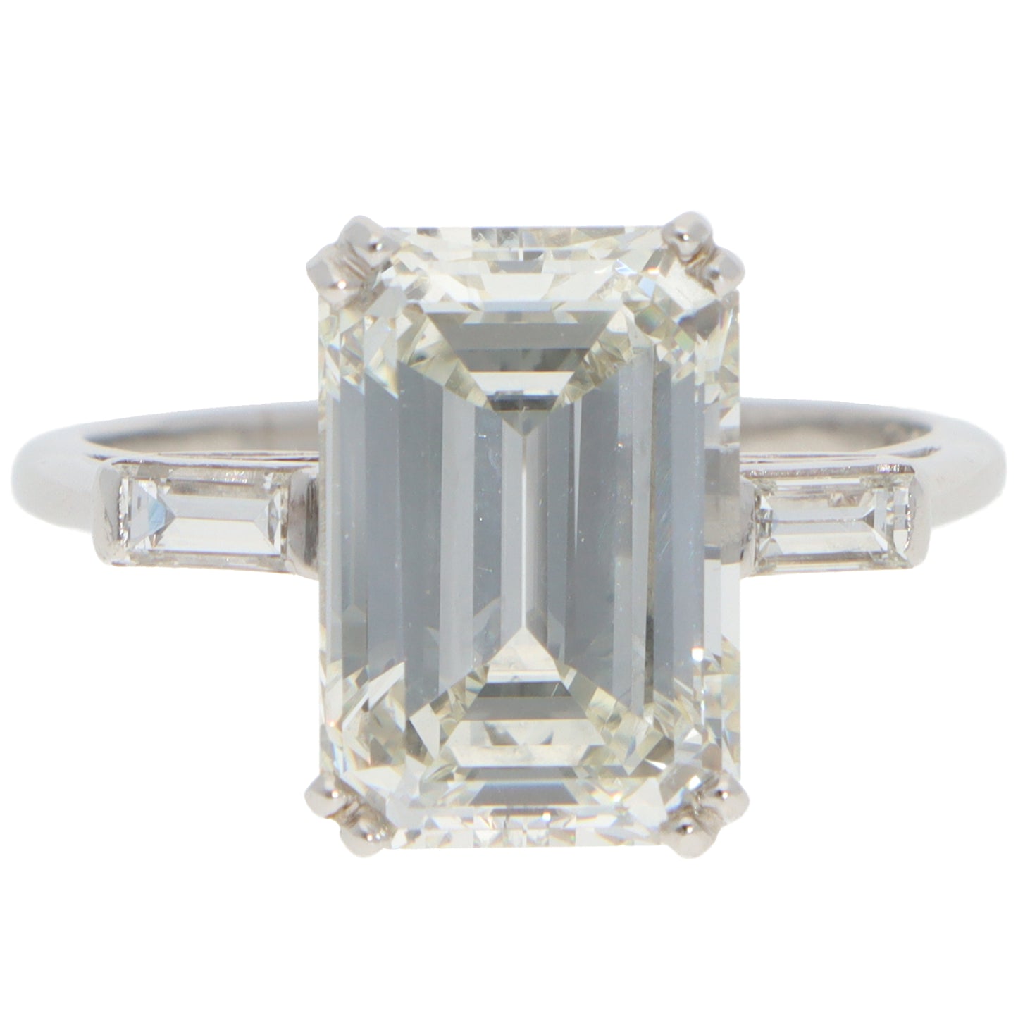 A large emerald cut diamond ring with baguette cut diamond shoulders in white metal, on a white background