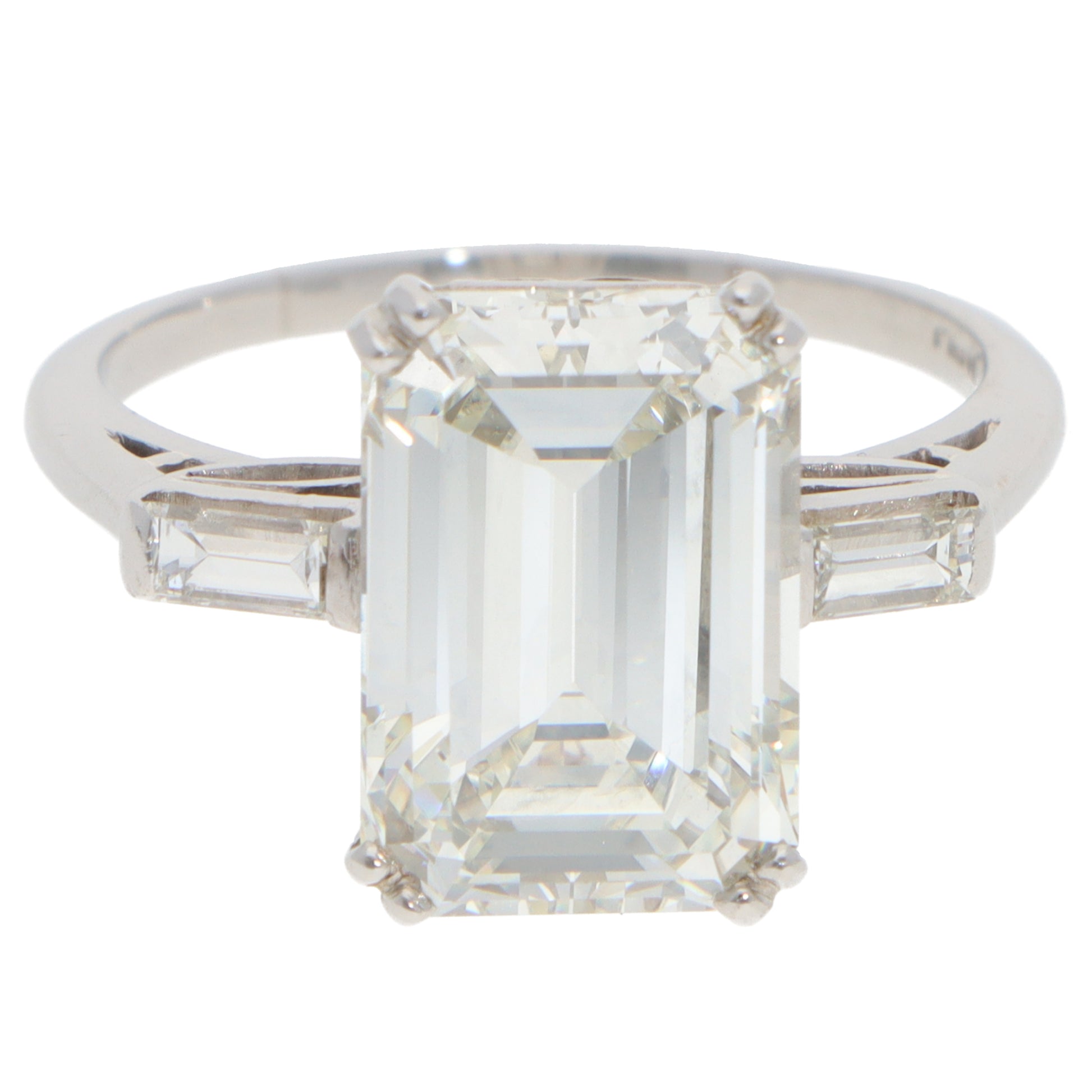 A large emerald cut diamond ring with baguette cut diamond shoulders in white metal, on a white background
