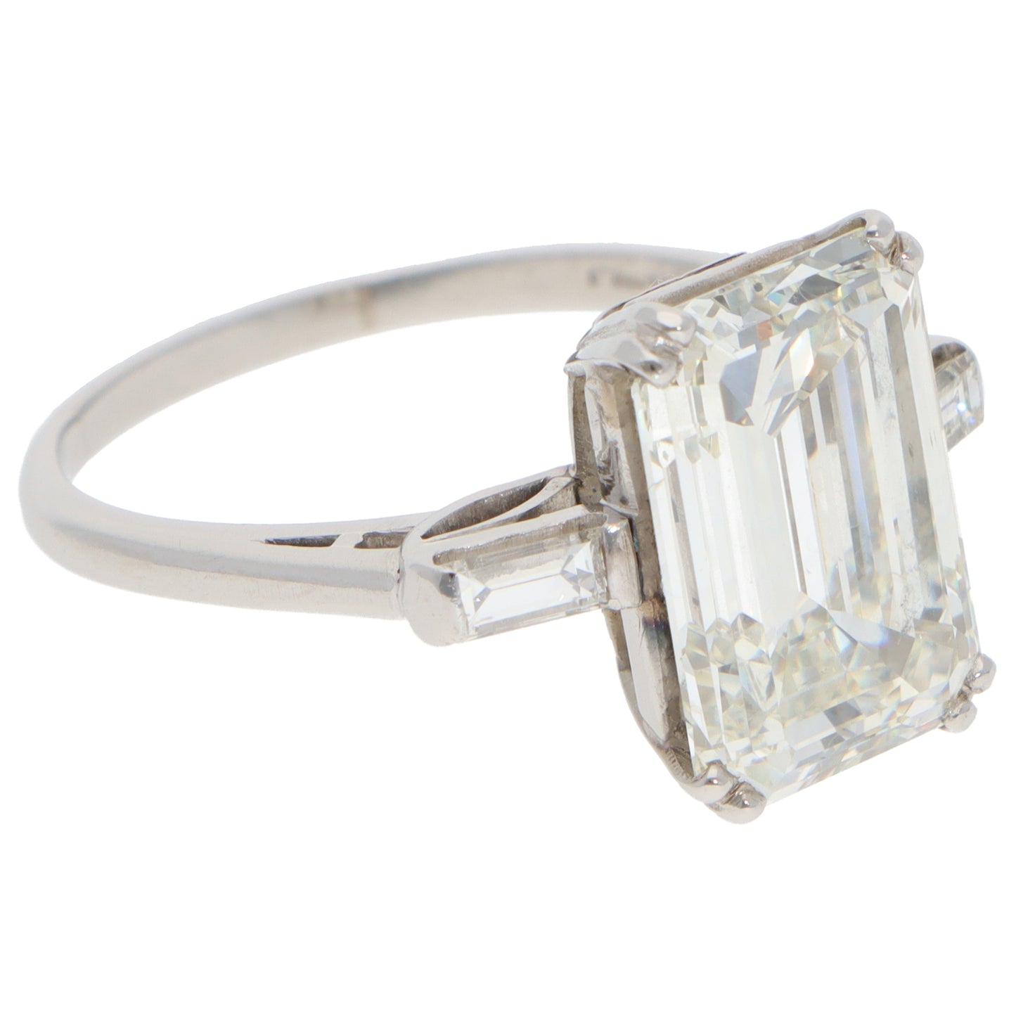 A large emerald cut diamond ring with baguette cut diamond shoulders in white metal, on a white background