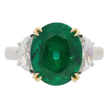 A three stone emerald and diamond ring in platinum and yellow gold, on a white background