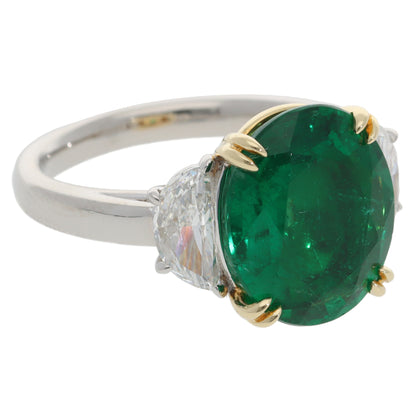 A three stone emerald and diamond ring in platinum and yellow gold, on a white background
