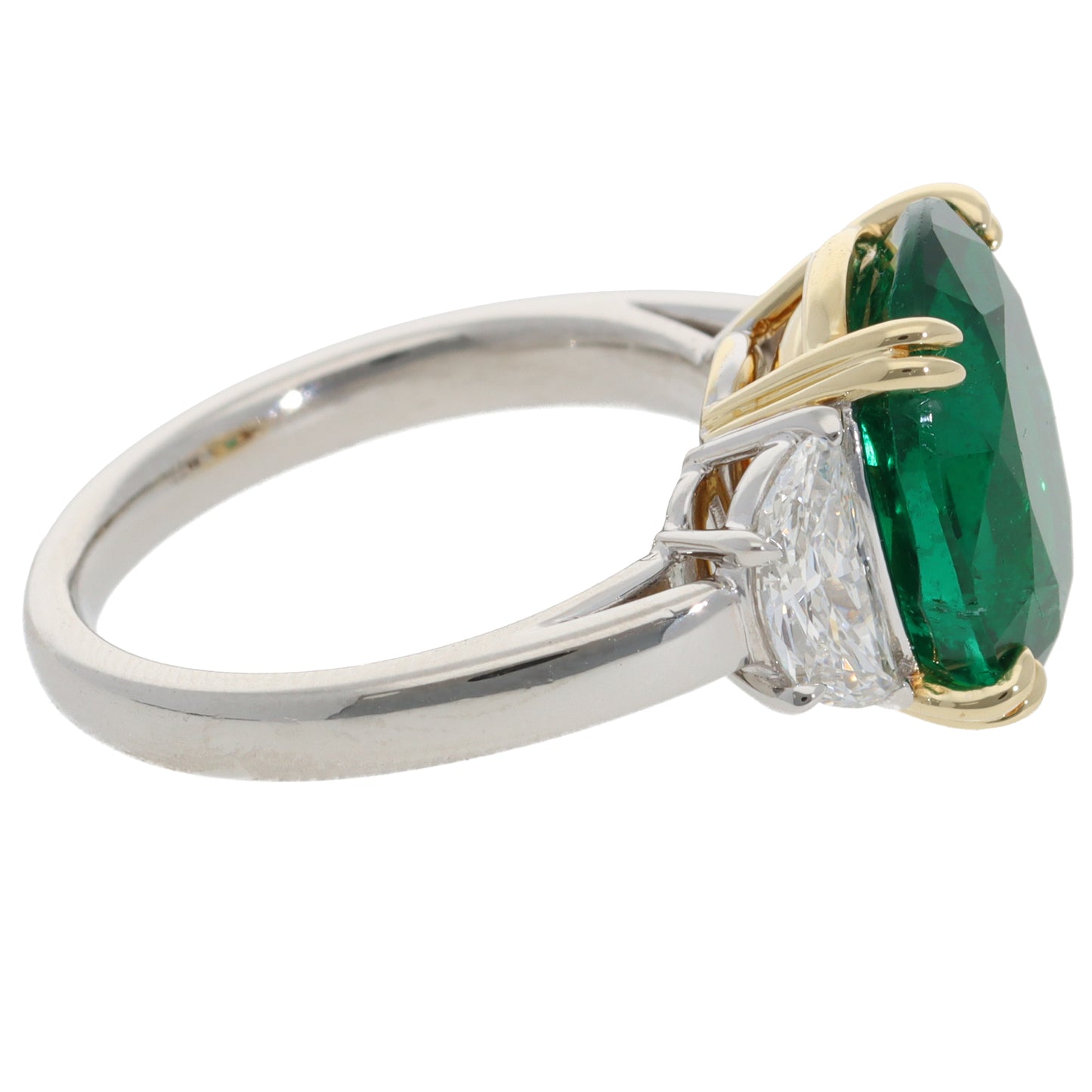 A three stone emerald and diamond ring in platinum and yellow gold, on a white background
