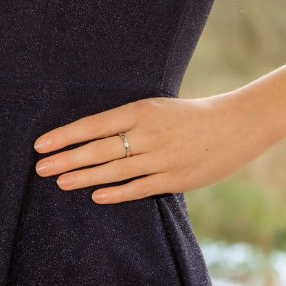 A white gold brilliant cut diamond eternity band, modelled by a woman wearing a black dress