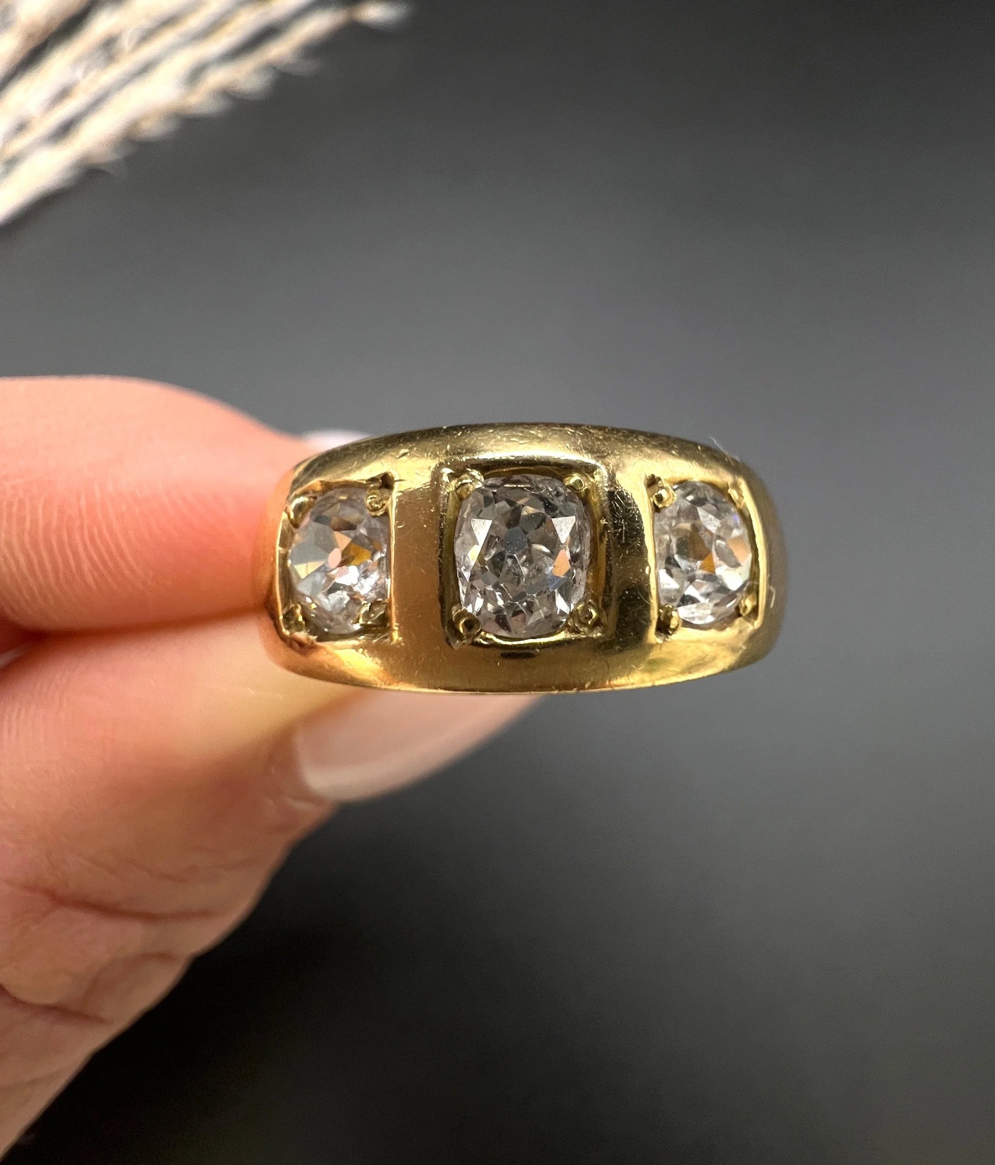A three stone old cut diamond ring in yellow gold, held in a hand