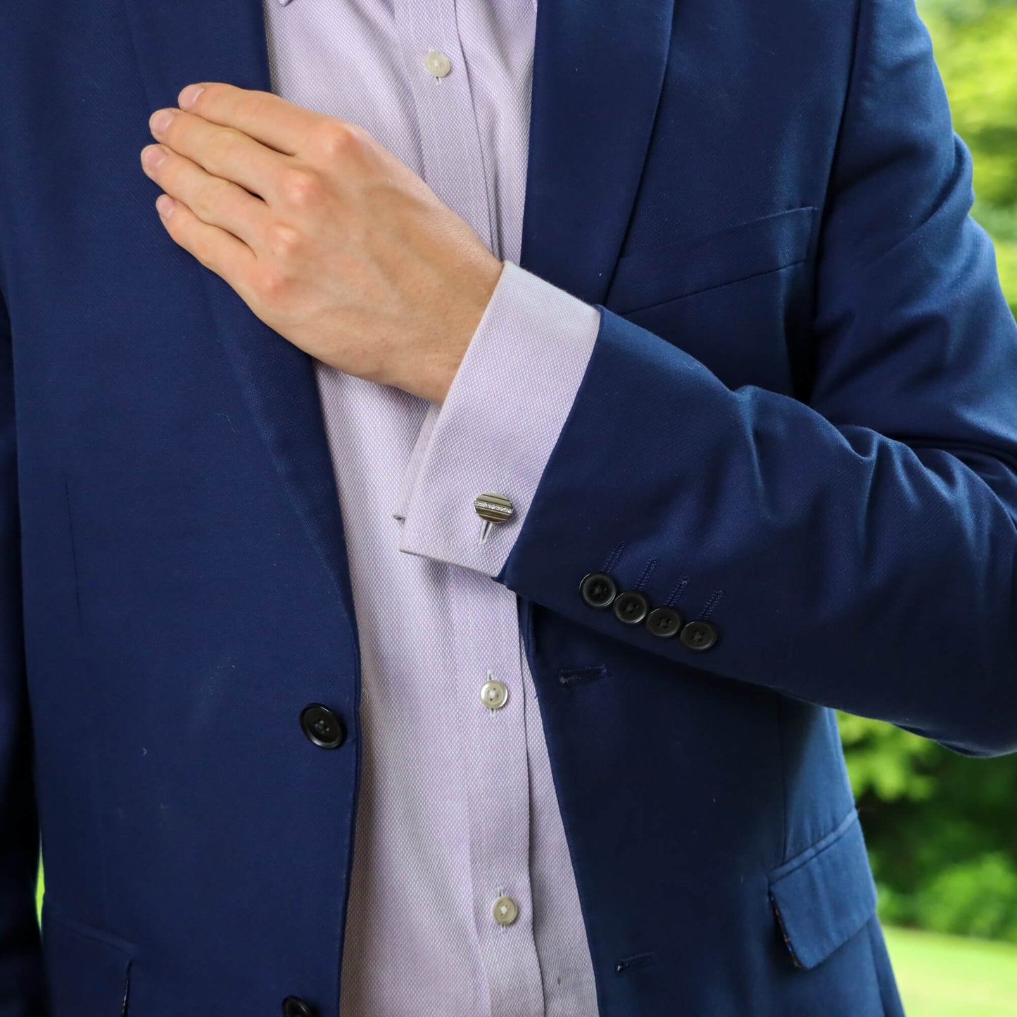 An oval cufflink in yellow and white metal set with diamonds, modelled by a man wearing a blue shirt and blue suit