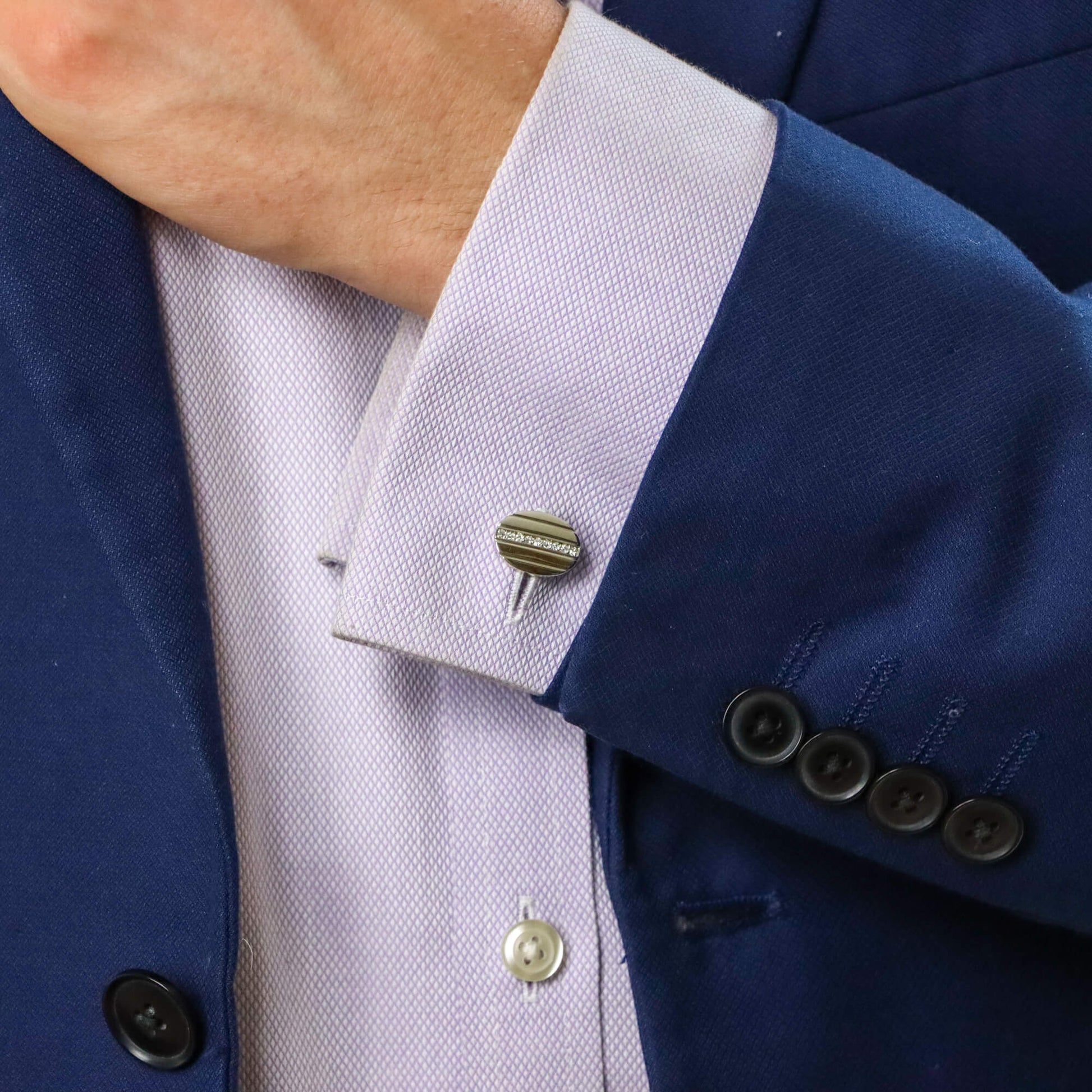 An oval cufflink in yellow and white metal set with diamonds, modelled by a man wearing a blue shirt and blue suit