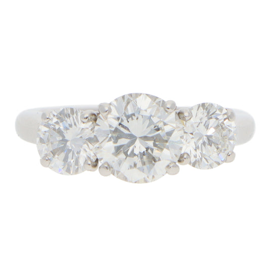 A three stone brilliant cut diamond claw set ring in white metal, on a white background