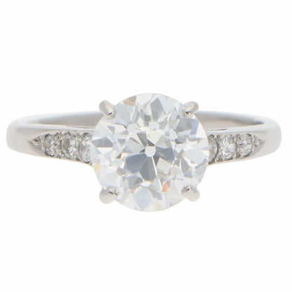 A round old cut diamond ring with diamond shoulders in platinum, on a white background