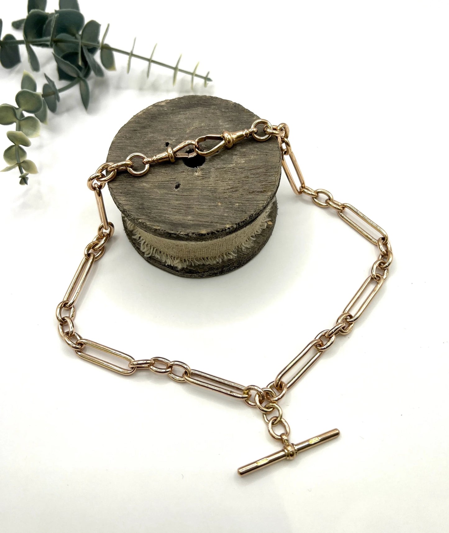 A rose gold trombone and fetter link Albert chain lying on top of a wooden object, on a white background