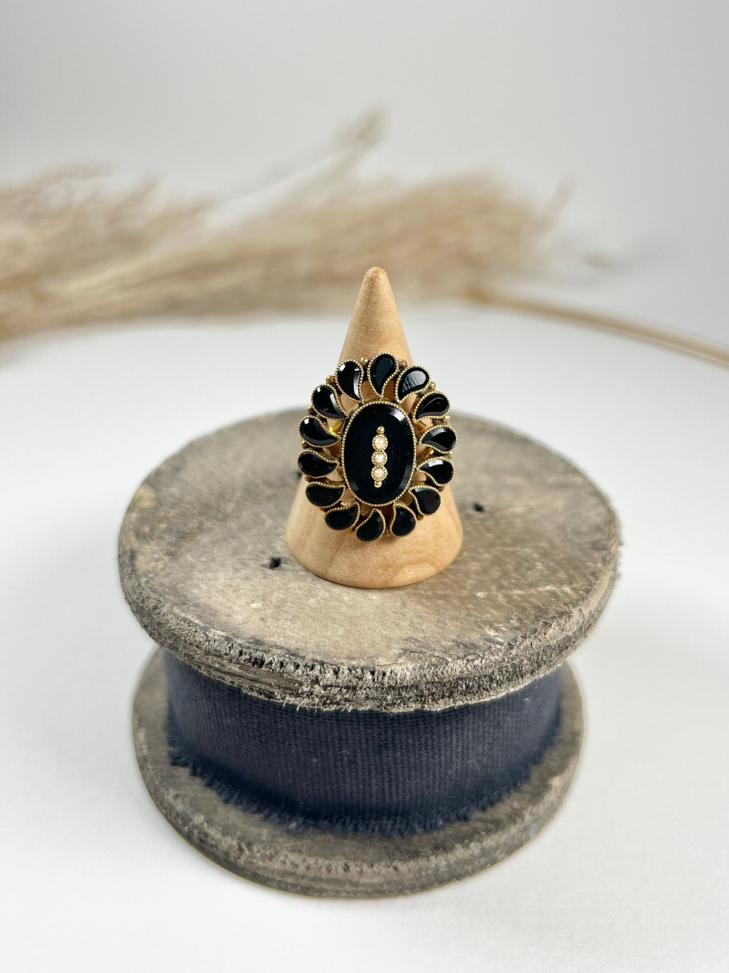 A black onyx and seed pearl fancy halo cluster ring in yellow gold, on a ring cone