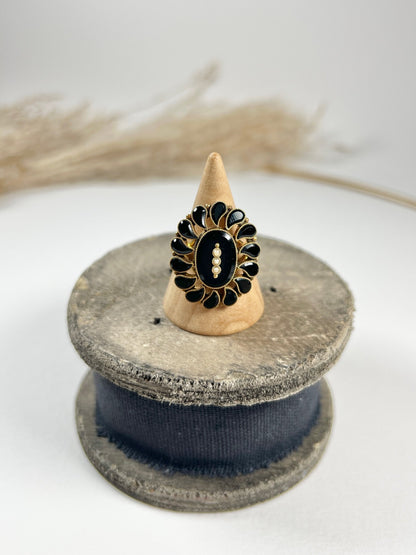 A black onyx and seed pearl fancy halo cluster ring in yellow gold, on a ring cone