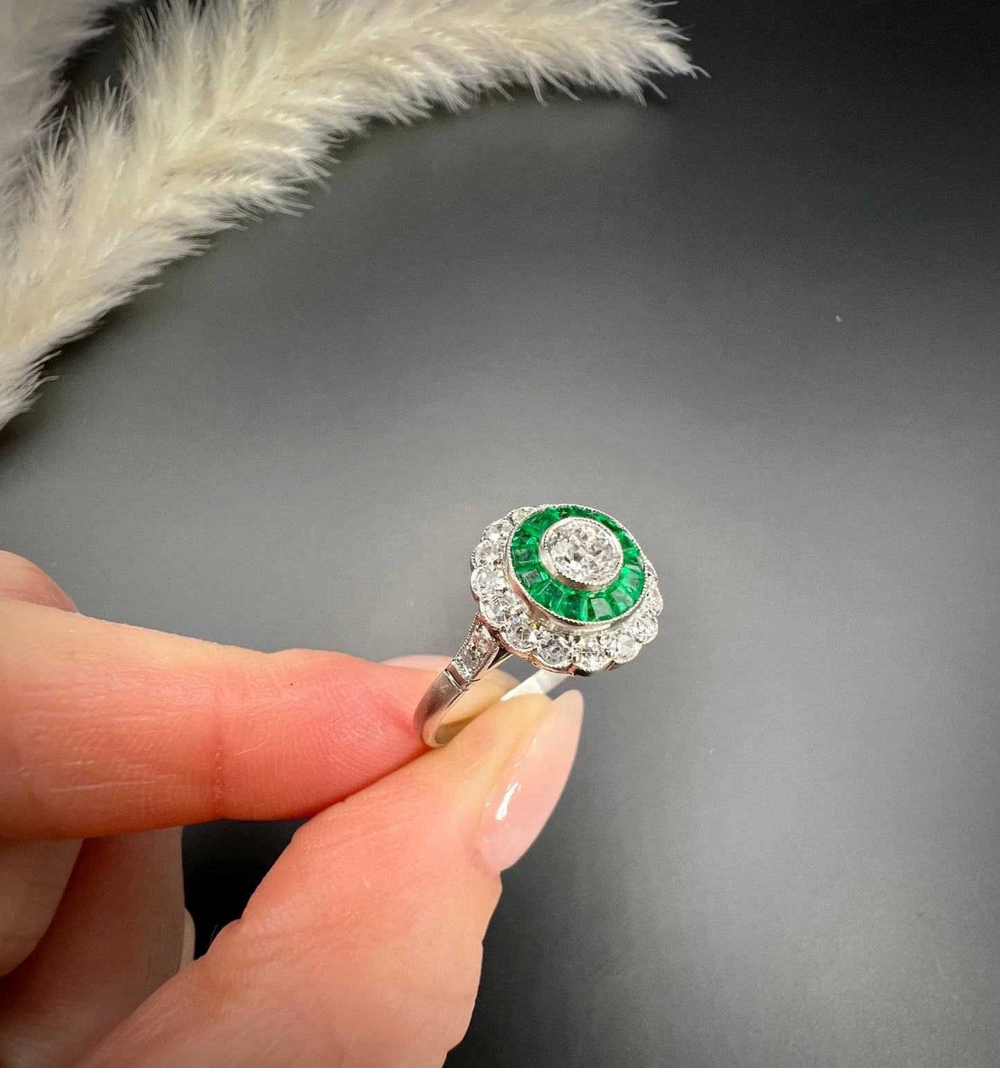 An emerald and diamond target cluster ring in platinum, held in a hand