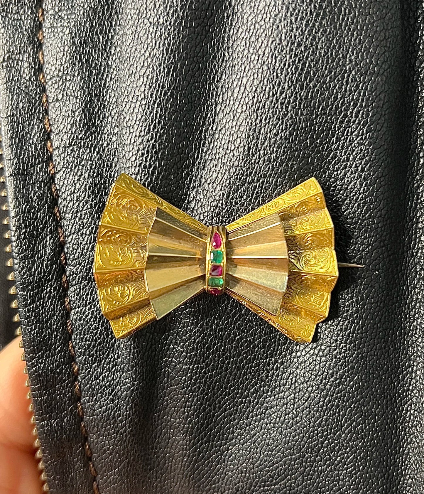 A yellow gold bow shaped brooch with rubies and emeralds, on a black jacket