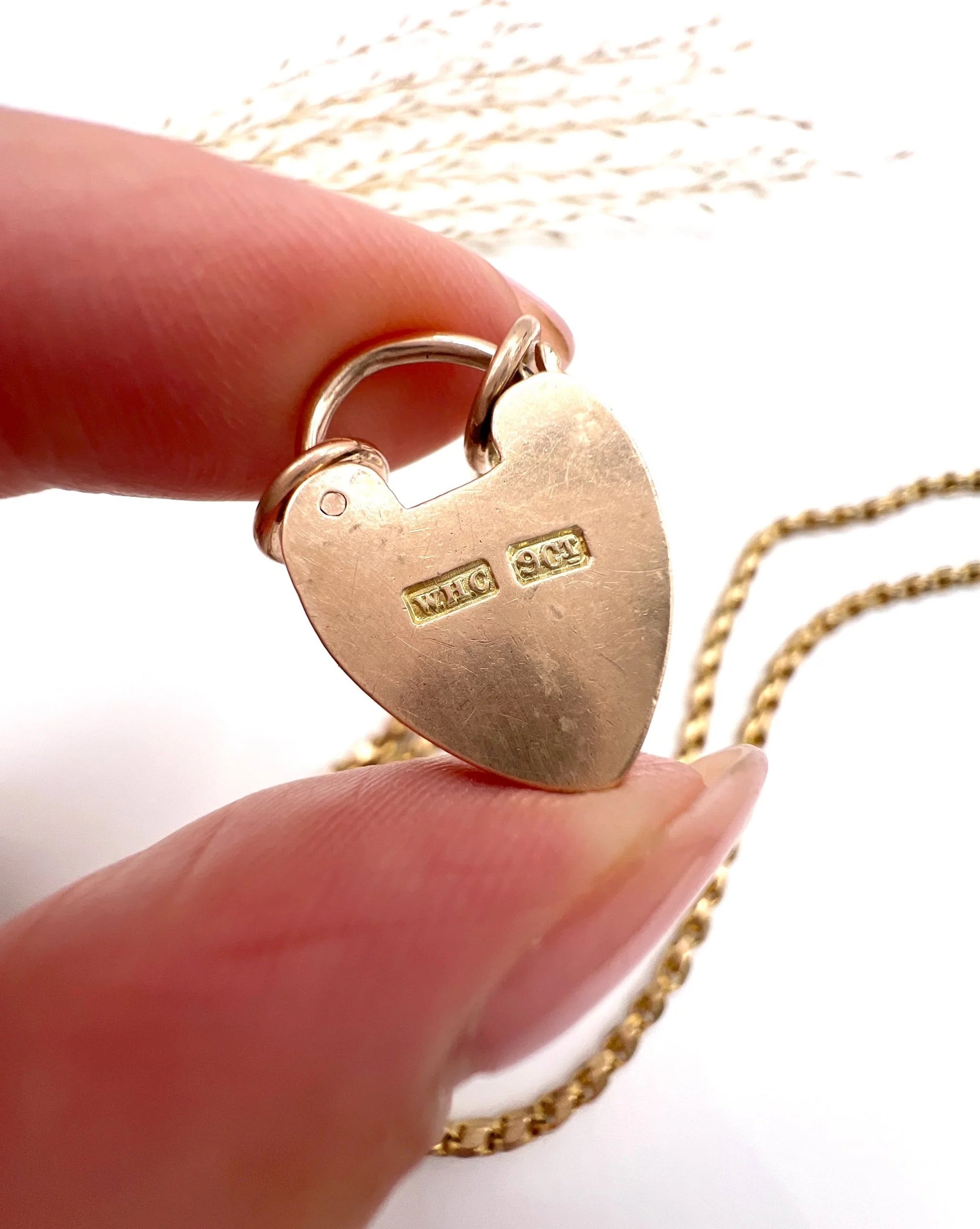 A close-up of a gold heart padlock with stamps, held in a hand
