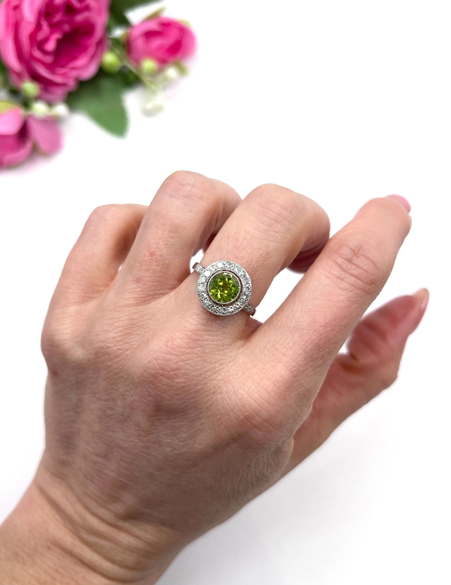 A white gold circular target cluster ring with a peridot centre surrounded by diamonds, modelled on a hand