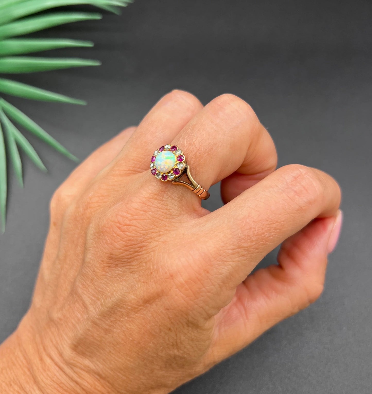 A daisy style cluster ring in rose gold with opal, ruby and diamond, modelled on a hand