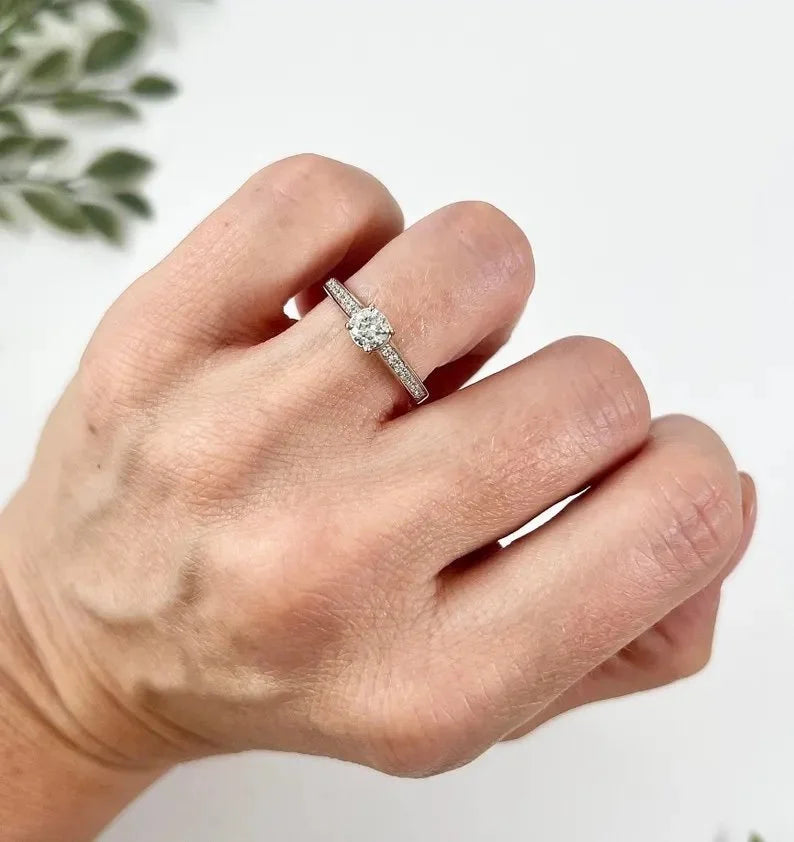 A white gold brilliant cut diamond engagement ring with diamond set shoulders, modelled on a hand