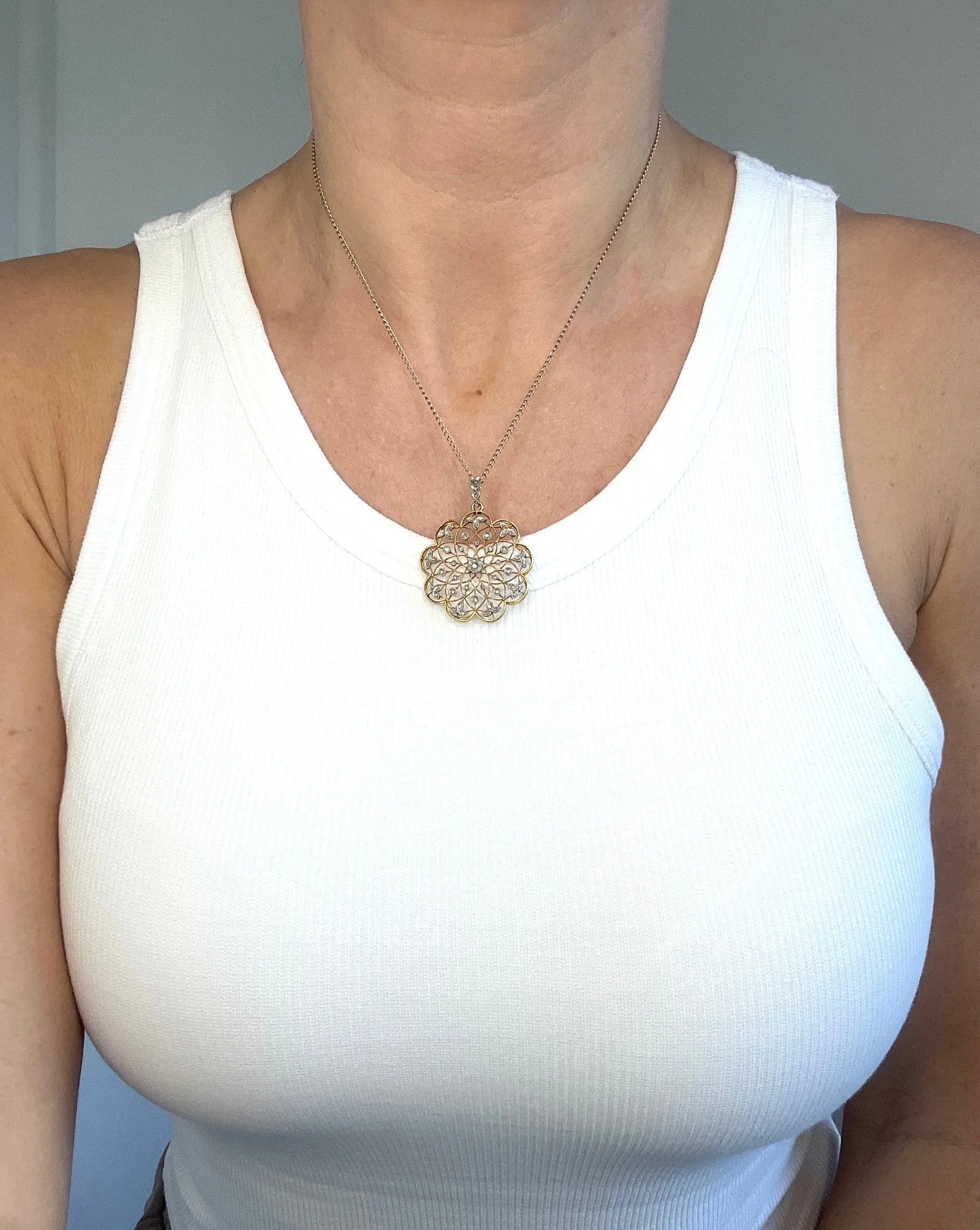 A floral openwork diamond pendant in gold and platinum, with a chain, modelled by a woman wearing a white top