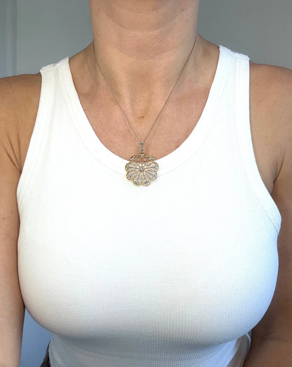 A floral openwork diamond pendant in gold and platinum, with a chain, modelled by a woman wearing a white top