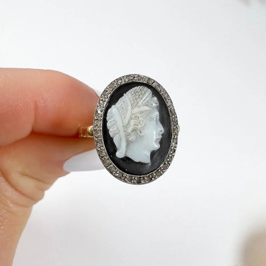 An oval cameo portrait ring with a diamond border mounted in gold, held in a hand