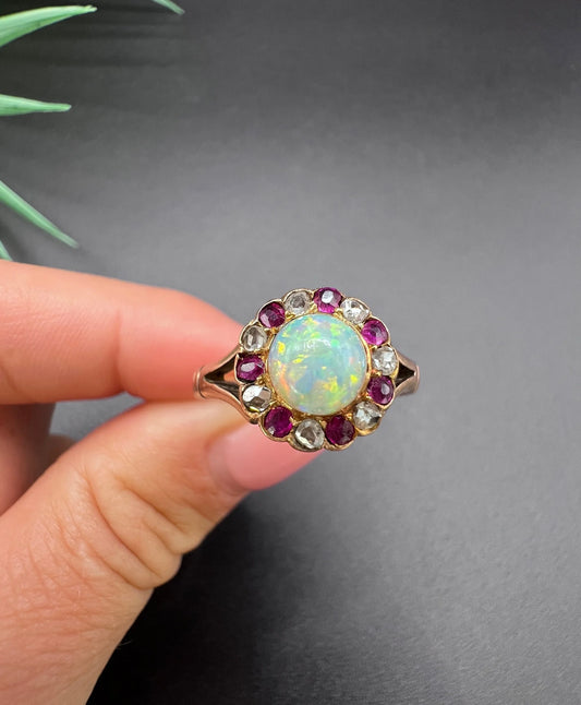 A daisy style cluster ring in rose gold with opal, ruby and diamond, held in a hand