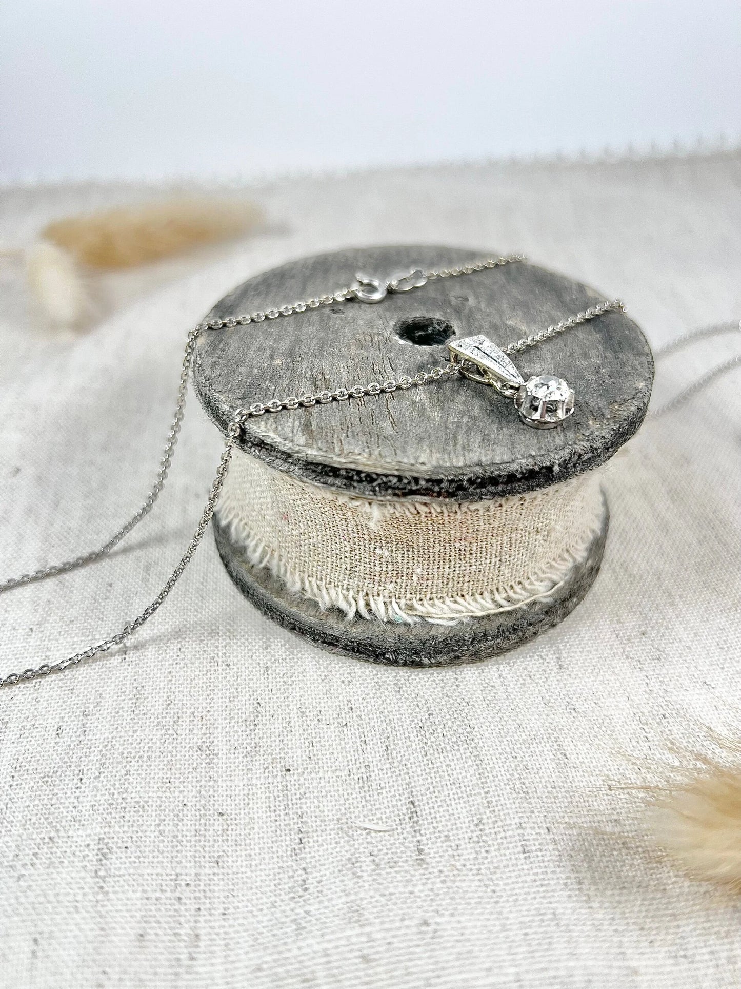 An old cut diamond pendant in white metal with a matching chain, on a circular wooden object