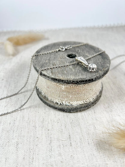 An old cut diamond pendant in white metal with a matching chain, on a circular wooden object