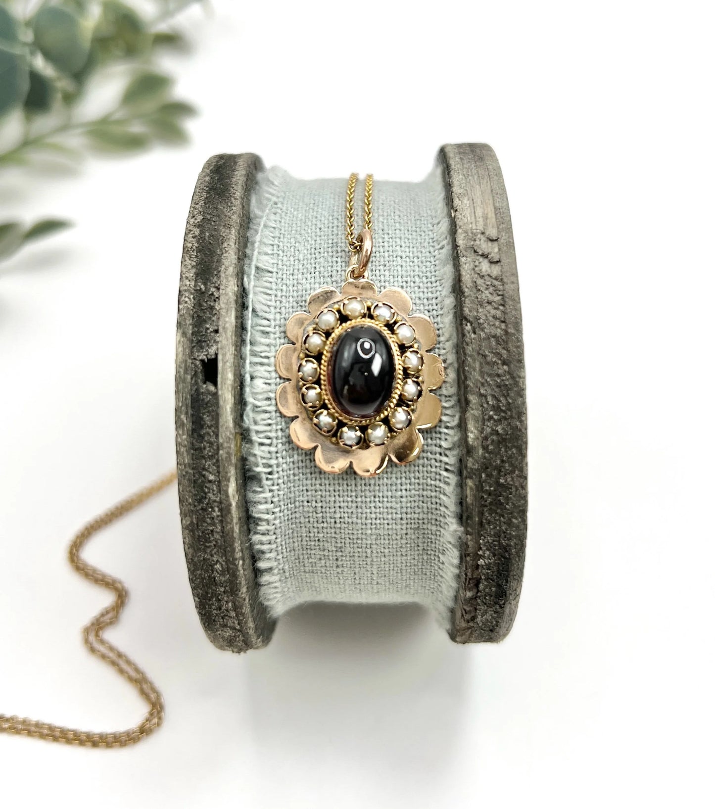 A cabochon garnet pendant with a seed pearl border in rose gold, with a chain