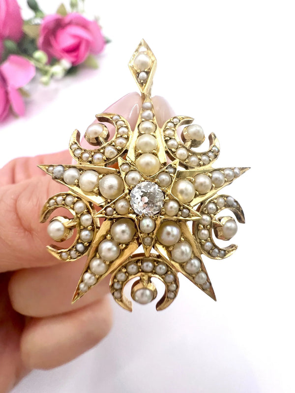 A yellow gold star and crescent brooch/pendant with pearls and a diamond centre, held in a hand