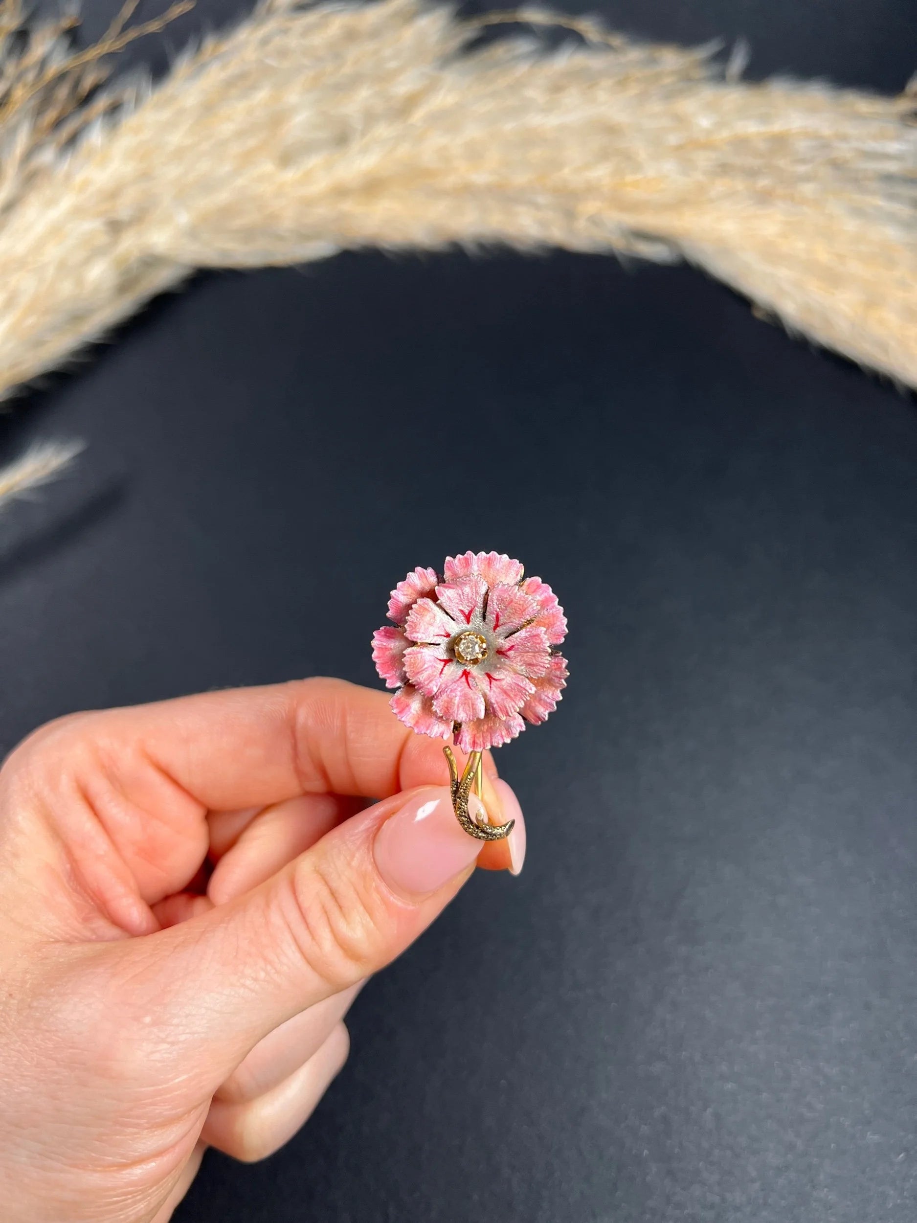 A pink enamelled flower brooch with a diamond centre, in yellow gold, held in a hand