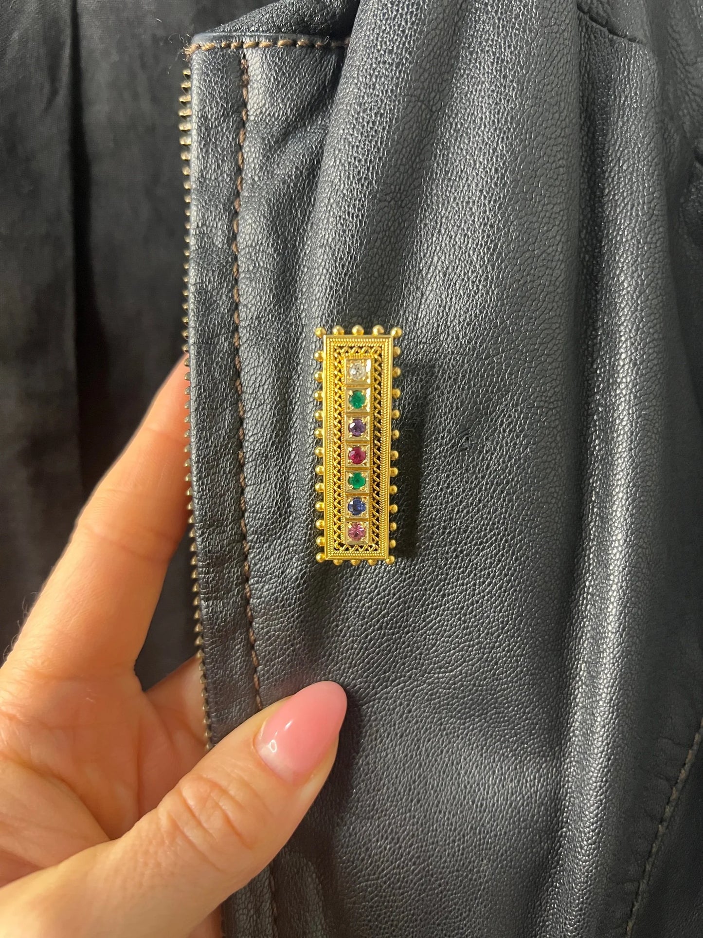 A yellow gold multi-gemstone and diamond acrostic brooch, on a black jacket