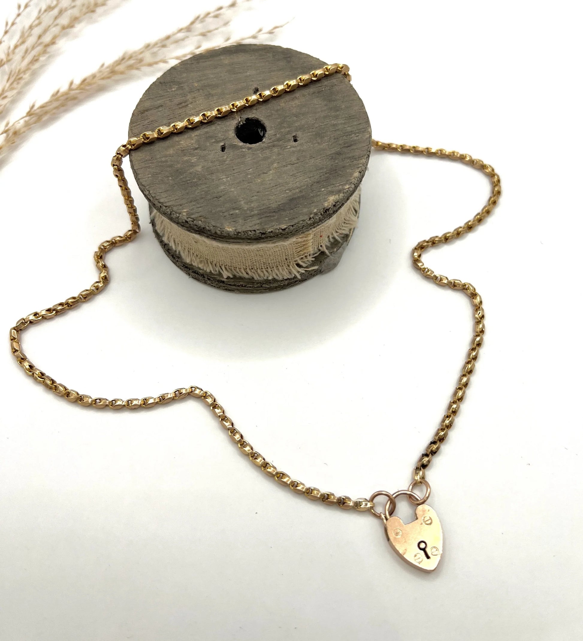 A gold chain necklace with gold heart padlock, on a wooden spool