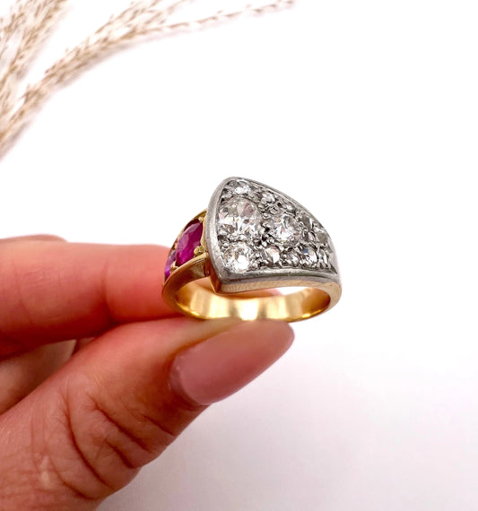 A diamond and ruby buckle design ring in gold and platinum, held in a hand