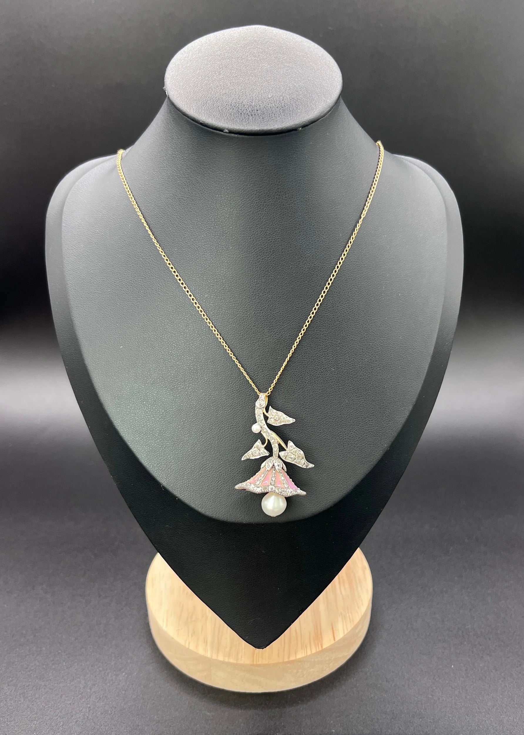 A pink enamel, diamond and pearl flower pendant in gold and silver, with a chain, modelled on a black jewellery bust