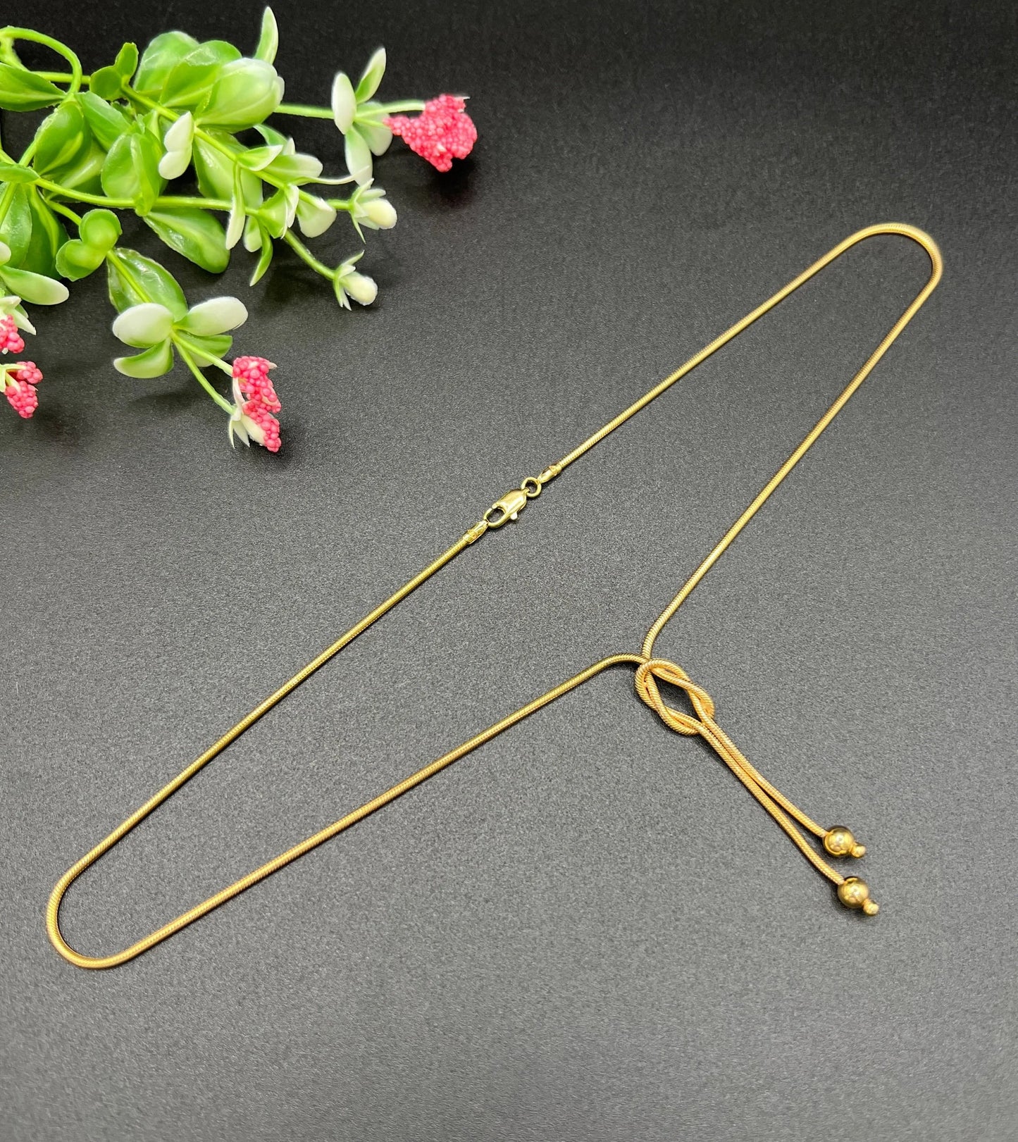 A yellow gold snake link chain necklace with a knot and tassel drop