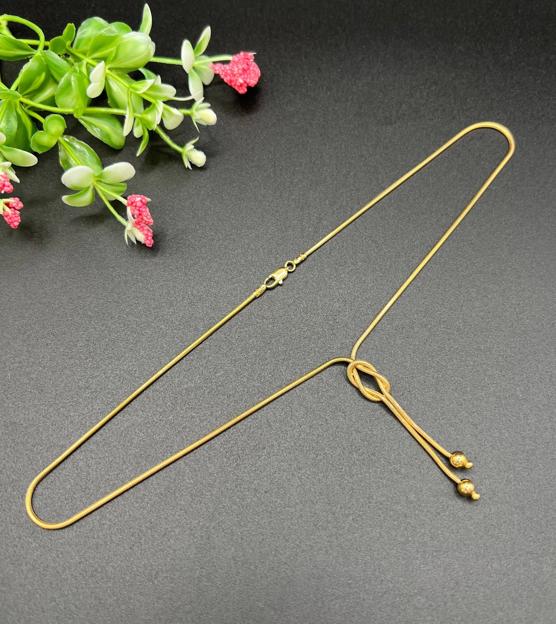 A yellow gold snake link chain necklace with a knot and tassel drop