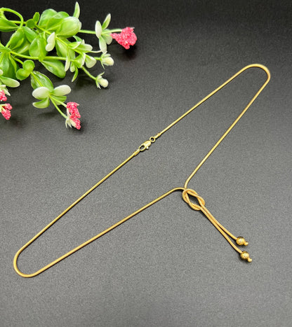 A yellow gold snake link chain necklace with a knot and tassel drop