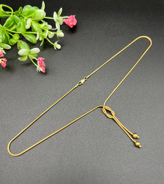 A yellow gold snake link chain necklace with a knot and tassel drop