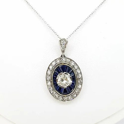 Sapphire and Diamond Oval Cluster Pendant on Diamond Set Chain; central brilliant cut diamond surrounded by calibre cut sapphires and an outer halo of diamonds