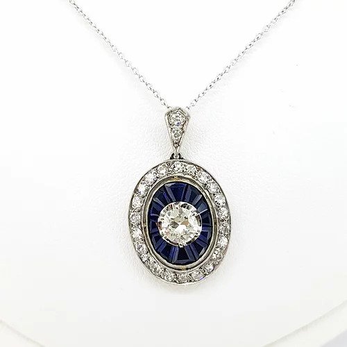 Sapphire and Diamond Oval Cluster Pendant on Diamond Set Chain; central brilliant cut diamond surrounded by calibre cut sapphires and an outer halo of diamonds