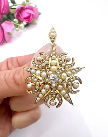 A yellow gold star and crescent brooch/pendant with pearls and a diamond centre, held in a hand