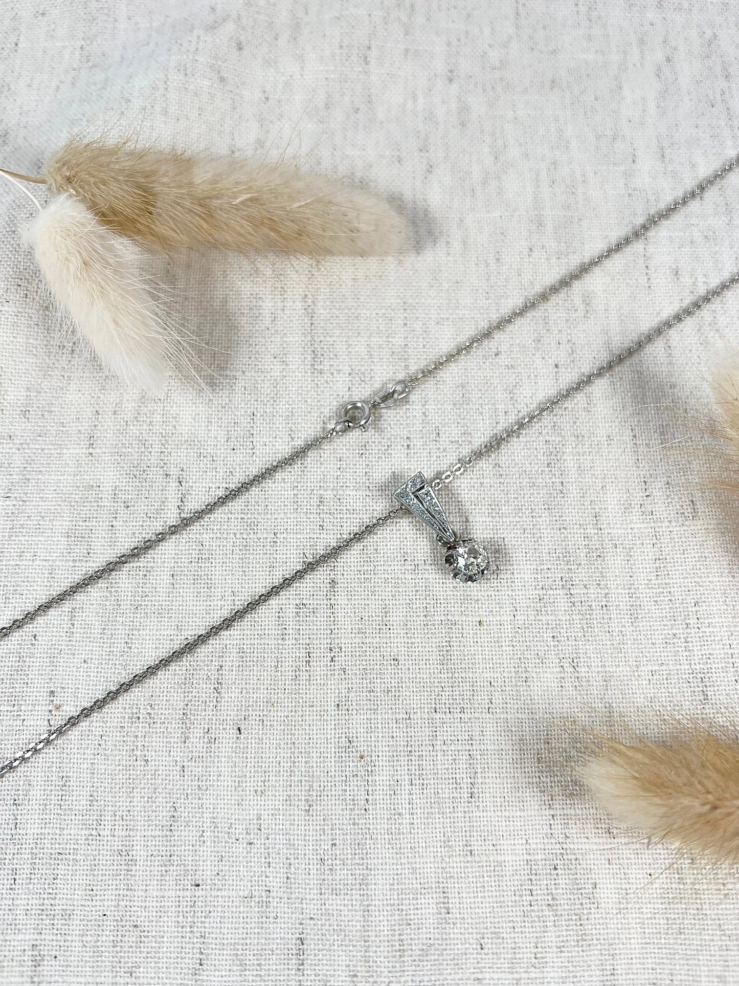 An old cut diamond pendant in white metal with a matching chain, on a fabric background