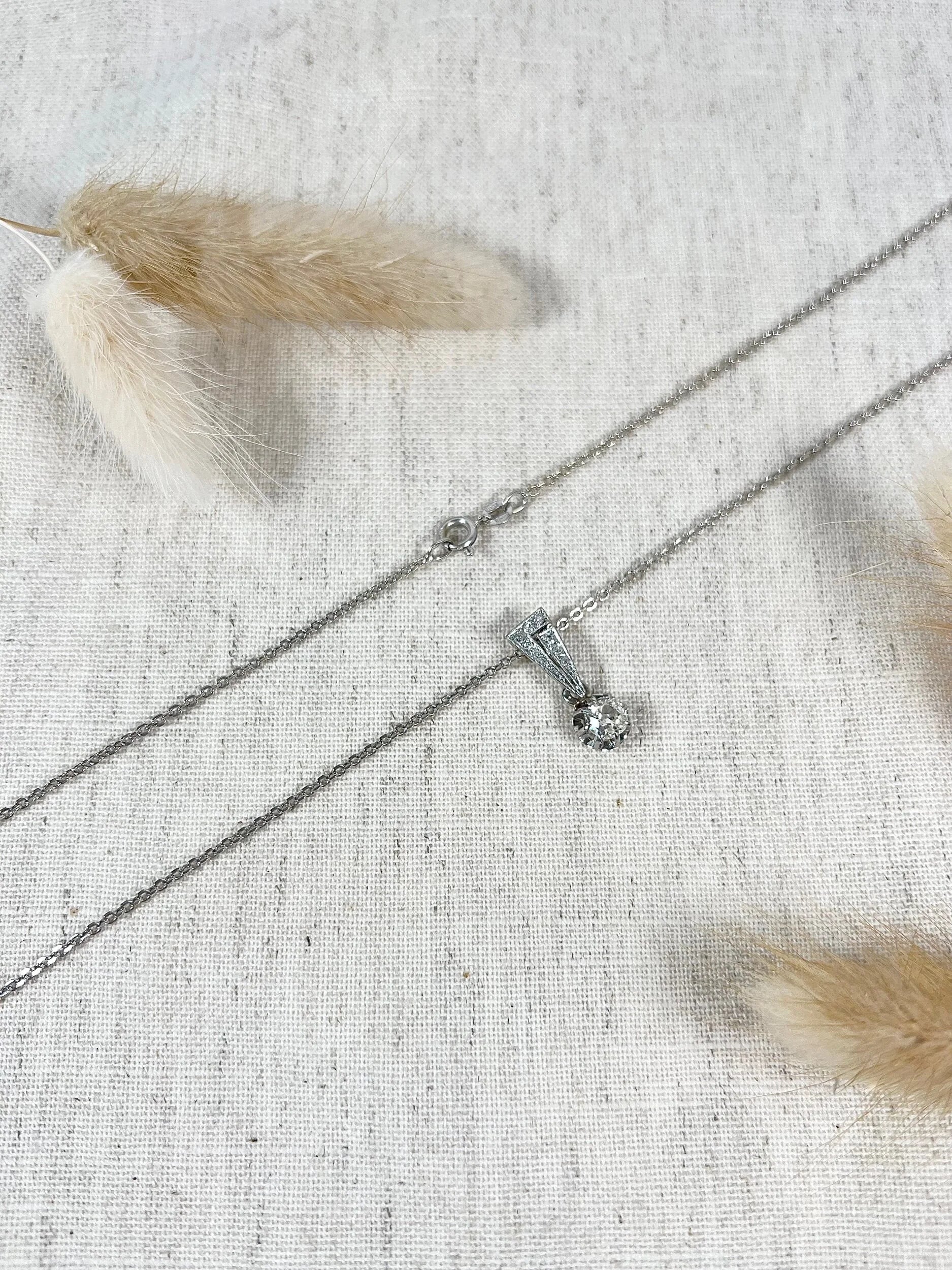 An old cut diamond pendant in white metal with a matching chain, on a fabric background