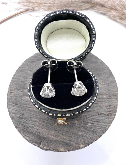 A pair of single stone round diamond stud earrings claw set in platinum, in a black jewellery box