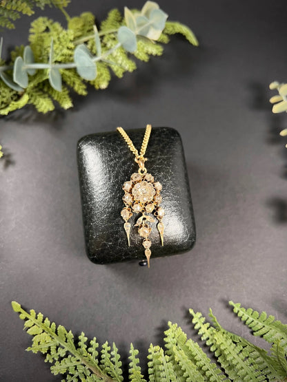 A yellow gold pendant with old cut diamonds, with a gold chain, on a black antique box